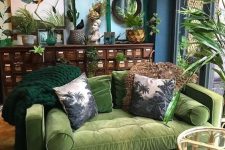 a moody tropical living space with blue walls, a vintage sideboard, a green sofa, a printed rug and bold artworks