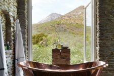 a natural rustic bathroom clad with stone and with a lovely copper bathtub in front of the window is a dream