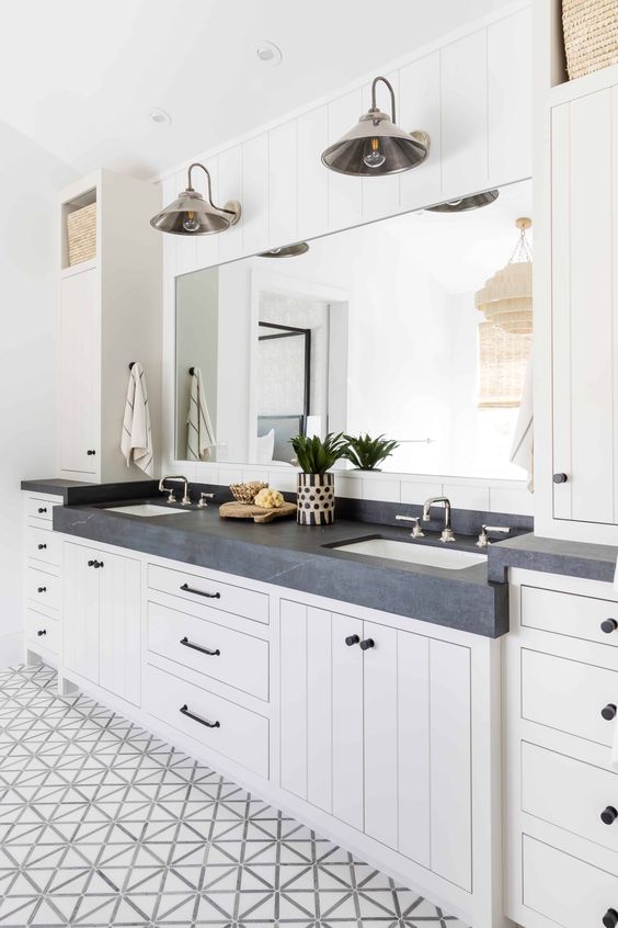 a nautical bathroom with a printed tiled floor, a large white shiplap vanity and cabinets, a black marble countertop, a mirror and sconces