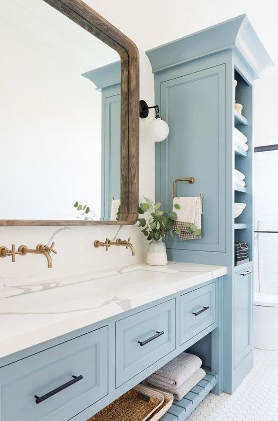 a neutral bathroom with light blue furniture, white marble, white hex tiles and a large mirror in a wooden frame