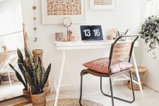 a neutral boho home office with a gallery wall, a small desk, a pink chair, layered rugs and potted greenery