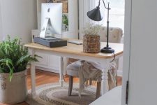 a neutral farmhouse home office with a vintage desk, a black table lamp and a computer stand, a vintage chair and lots of ferns