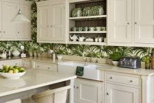 a neutral farmhouse kitchen with creamy cabinets, tropical print wallpaper, creamy woven chairs and pendant lamps