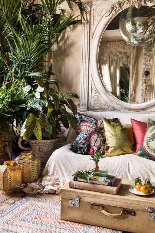 a neutral yet moody living room with neutral walls, a neutral sofa, a vintage suitcase as a coffee table and potted plants plus a vintage mirror