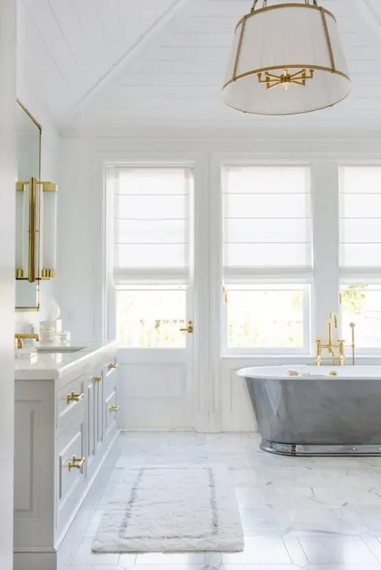 a refined coastal bathroom with a marble floor, a metal clad tub, a large vanity and gold touches and fixtures