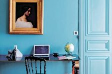 a refined eclectic blue home office with a chic desk, a velvet chair, a vintage artwork and modern accessories