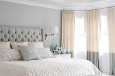 a refined grey bedroom with dove grey walls, a grey bed and bench, color block curtains and a crystal chandelier