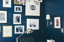 a refined modern navy home office with a gallery wall, a glass desk, a leather chair and chic lamps