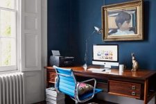 a refined navy home office with a vintage rich stained desk, a modenr blue chair, a cowhide rug, a vintage artwork and a simple lamp