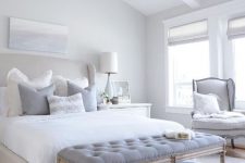 a relaxing dove grey bedroom with a grey upholstered bed, grey upholstered furniture, a vintage chandelier and a coastal artwork