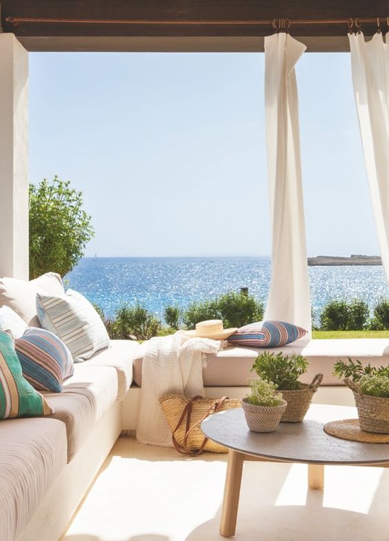 a romantic coastal porch with a large L shaped sofa, colorful linens, curtains for privacy and a fantastic sea view