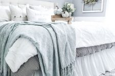 a romantic modern farmhouse bedroom with light blue wlals, a white leather bed, chic neutral and light blue bedding and a shelf with pumpkins and cascading greenery
