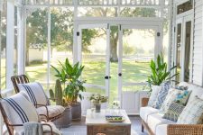 a screened beach porch with rattan and wicker furniture, printed textiles, a wooden table and a blue rug plus potted plants