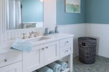 a sea farmhouse bathroom with a large white vanity and a mirror, blue walls and light blue towels and touches