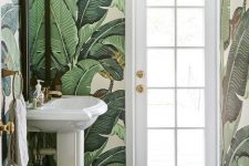a simple and small powder room with banana leaf wallpaper, white appliances and touches of gold