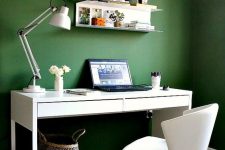 a simple and stylish contemporary home office with green walls, white furniture and a basket as a trash bin