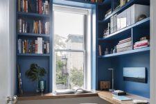 a small blue home office with shelves that take the whole space, a floating wooden desk and a white chair