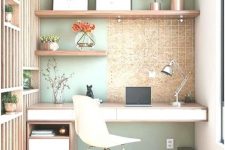 a small home office nook with a sage green wall, floating shelves and a desk, a white chair and a wood slab divider