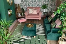 a small tropical living room with a tropical leaf wall, a green sofa and ottoman, a pink chair, touches of gold