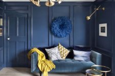 a sophisticated living room with navy paneled walls, a blue sofa, a gold chandelier and lamps and mustard accents