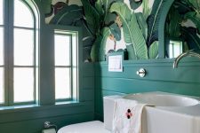 a statement tropical bathroom with banana leaf wallpaper on the ceiling, emerald panels and white appliances for a bold look
