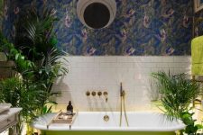 a statement tropical bathroom with moody wallpaper, a neon green tub and towels and potted greenery
