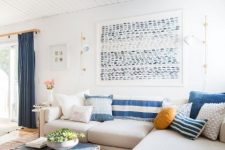 a stylish coastal living room with a corner sofa, indigo printed pillows, an indigo chest and a catchy seaside artwork