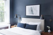 a stylish contemporary bedroom with navy walls, a white leather bed, wooden chests as nightstands and navy pillows