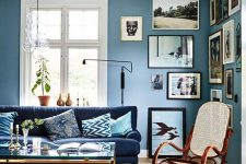 a stylish eclectic living room with blue walls, a navy sofa, a gallery wall and touches of gold for more chic