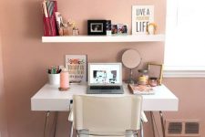 a stylish home office nook with a dusty pink wall, white furniture, open shelving and nothing unnecessary