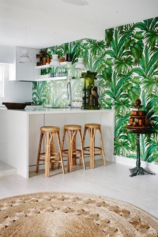 a stylish tropical kitchen with a tropical leaf wall, sleek white cabinets, rattan stools and a jute rugs reminds of beaches