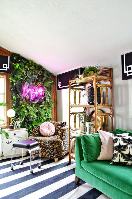 a super bold and fun home office with a greenery wall with a neon light, an emerald sofa, a leopard print chair and an acrylic stool