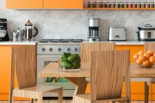 a super colorful kitchen with sleek orange cabinets, a marble backsplash and countertops, stained dining furniture and a colorful rug