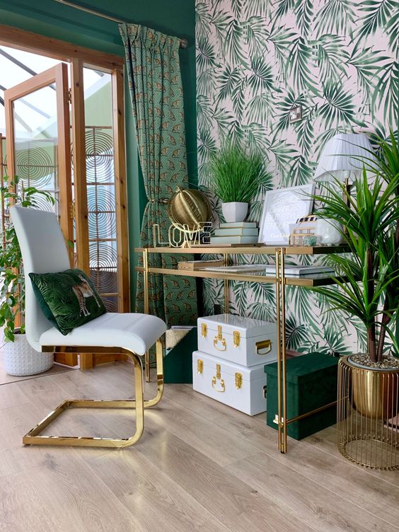 a tropical home office with a leaf accent wall, printed green curtains, lots of plants and boxes and much gold for a glam feel