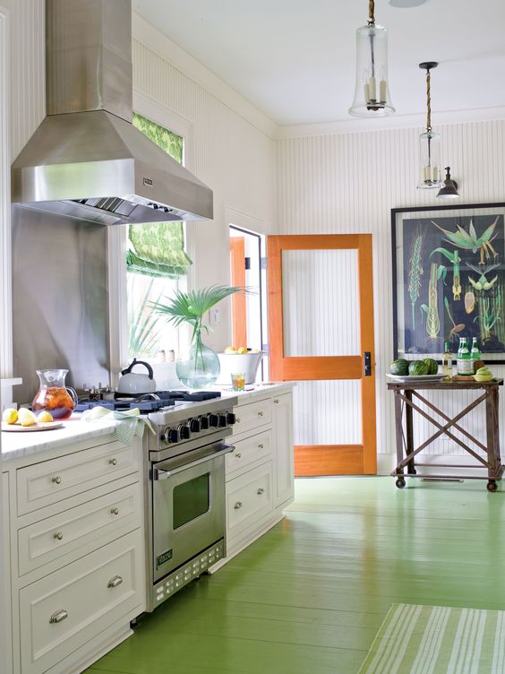 a vibrant tropical kitchen with a green floor, an orange door, white cabinets, a bright tropical wall art