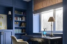 a vintage-inspired blue home office with built-ins and paneling, with a refined black desk and velvet chair and chic lamps