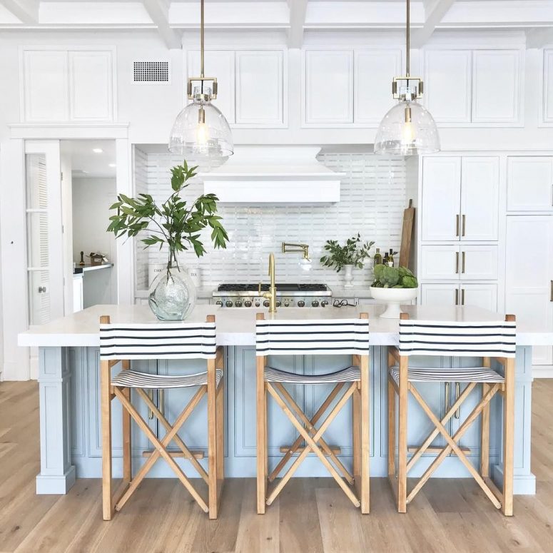 a vintage-inspired coastal kitchen with white cabinets, a light blue kitchen island, striped stools and glas spendant lamps