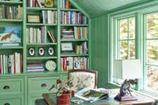 a vintage-inspired home office in sage green, with a rough wooden desk, a large wall storage unit taking the whole wall