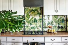 a vintage-inspired neutral tropical kitchen with large cabinets, tropical leaf wallpaper, touches of black for drama