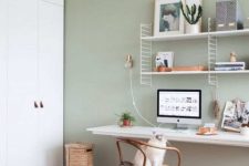 a welcoming and comfy home office with a pastel green accent wall, a floating desk, a shelving unit and white table and chairs