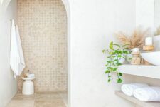 a welcoming beach bathroom with an arched entrance to the shower space, a wall-mounted vanity and sinks, wooden candleholders and grasses