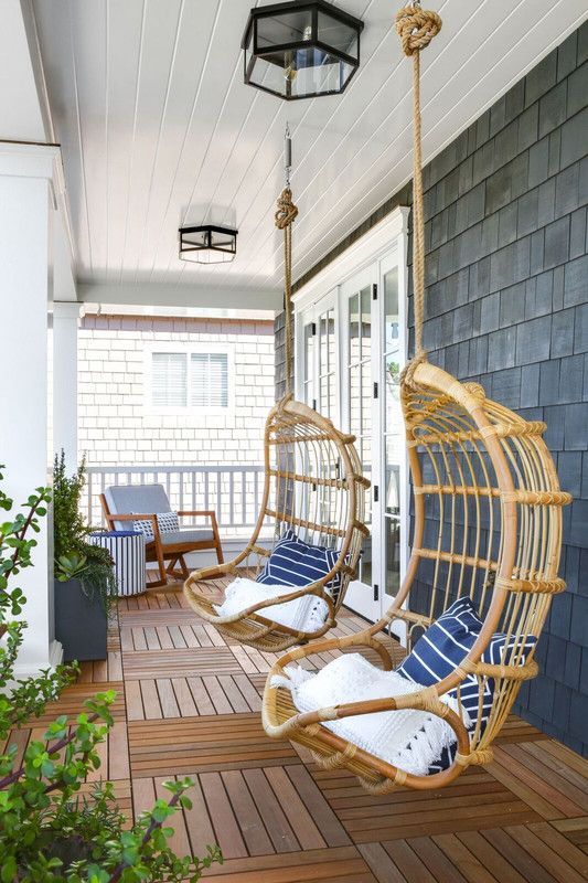 a welcoming beach porch with a blue chair and an ottoman and hanging rattan chairs with blue pillows