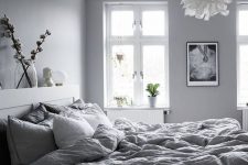 a welcoming grey Nordic bedroom with dove grey walls, grey bedding, a fluffy pendant lamp and catchy artworks
