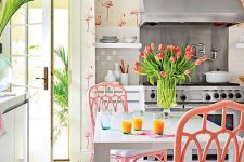 a whimsy tropical kitchen with flamingo wallpaper, white cabinets and a table, pink rattan chairs and blooms and greenery