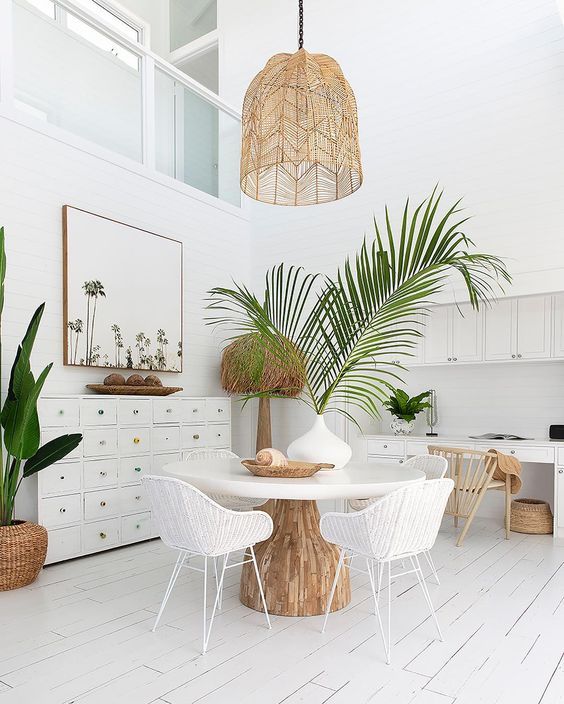 a white tropical home office with white furniture, woven and wooden chairs, a woven pendant lamp and potted plants
