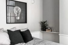 an airy grey Scandinavian bedroom with dove grey walls, grey and black bedding and a dark artwork plus pendant lamps