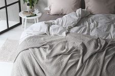 an airy grey bedroom with an upholstered dove grey bed, grey and blush bedding, a potted plant and touches of black