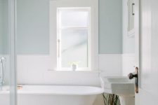 an airy retro-inspired coastal bathroom with color block pale blue and white walls, a clawfoot tub, a free-standing sink and neutral linens
