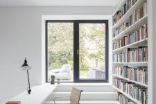 an airy white home office and library with an oversized bookshelf that divides spaces and a built-in desk