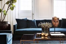 an elegant and laconic living room with white walls, blue furniture, glass tables and touches of gold for more chic